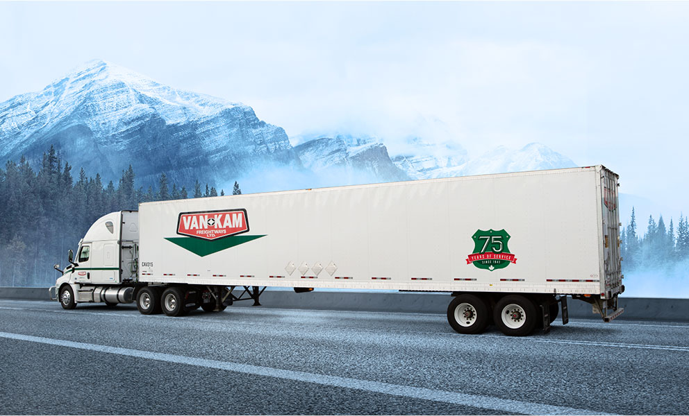 Van Kam highway truck driving in front of BC evergreen forest and snowy mountains