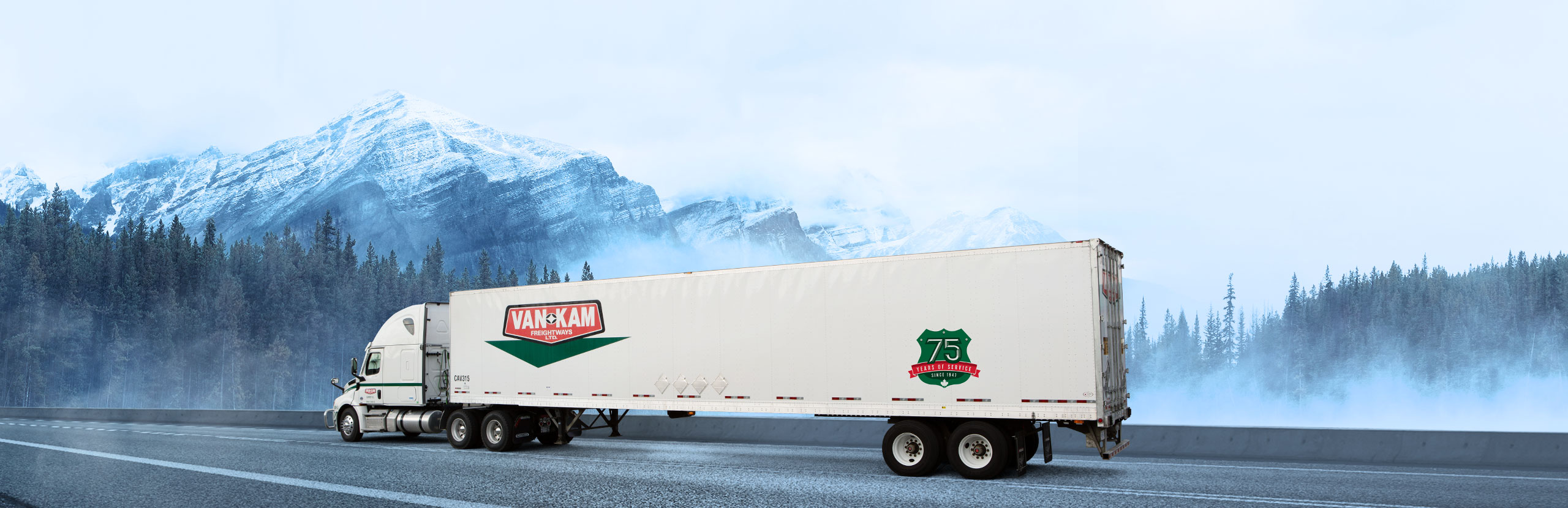 Van Kam highway truck driving in front of BC evergreen forest and snowy mountains